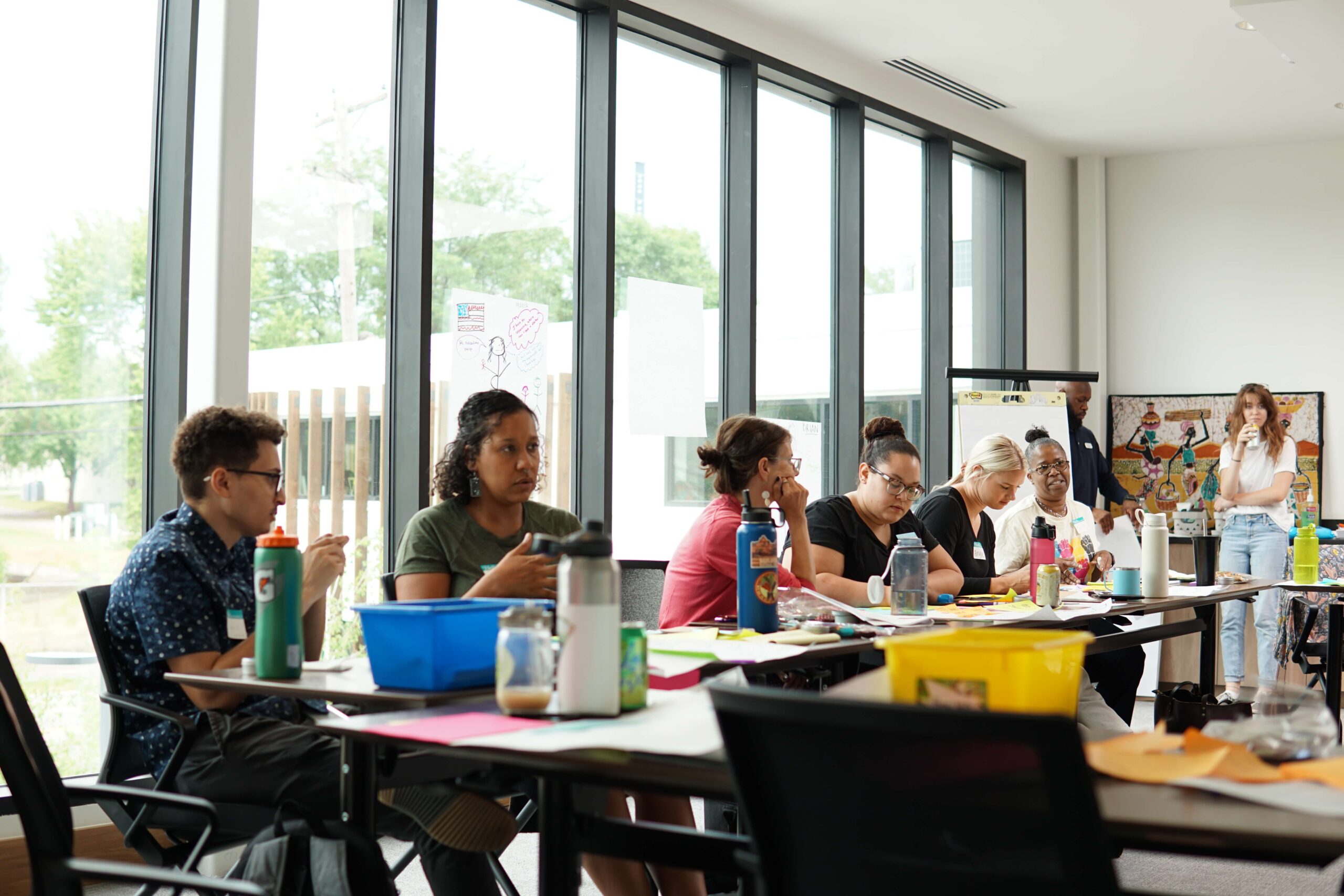 A group of adults sitting around tables in a bright room, participating in a workshop or meeting.