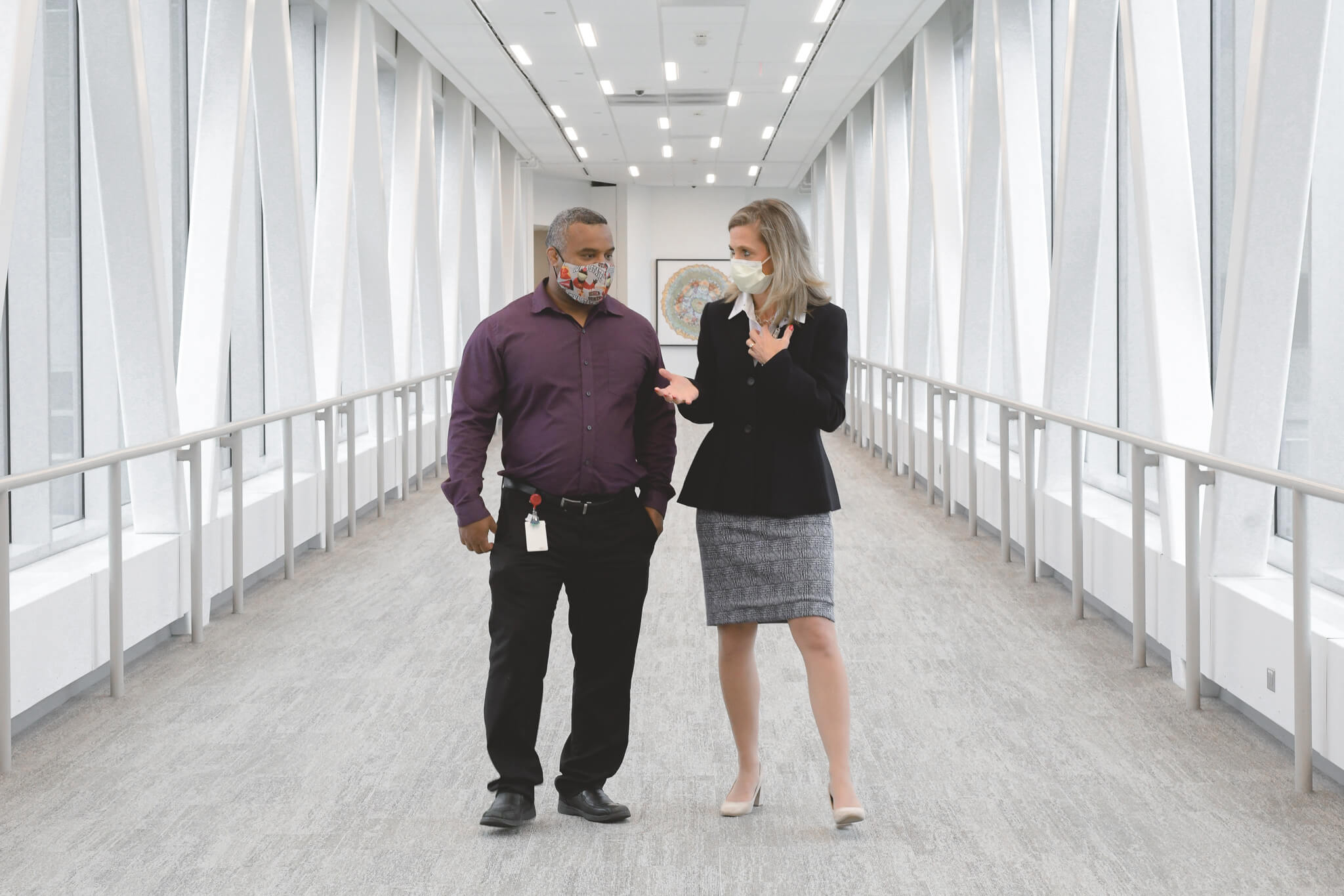 Two individuals having a discussion in a hallway while wearing face masks